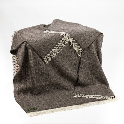 Dark Grey Herringbone blanket with white wool fringing on two ends. It has an organic appearance