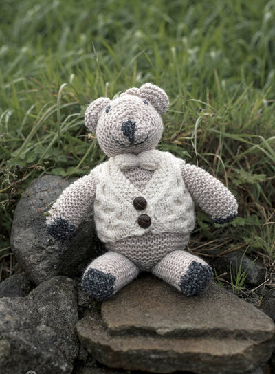Charlie the bear is handknkit . He wears a handknitted aran waistcoat fastening with 2 brown buttons . He wears a bow tie in natural to match the waistcoat . His body is oatmeal. 100% soft merino wool.