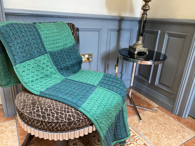 knitted wool Throw. Two tones, moss green and Kelly Green knitted to create a patchwork pattern of honeycomb and cable stitches in a patchwork pattern of the 2 greens 
